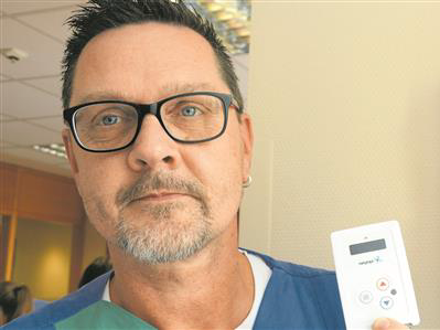 Ein Mann hält ein RTLS-Tag in der Hand, im Hintergrund befindet sich eine an der Wand montierte Ladestation mit weiteren Tags.