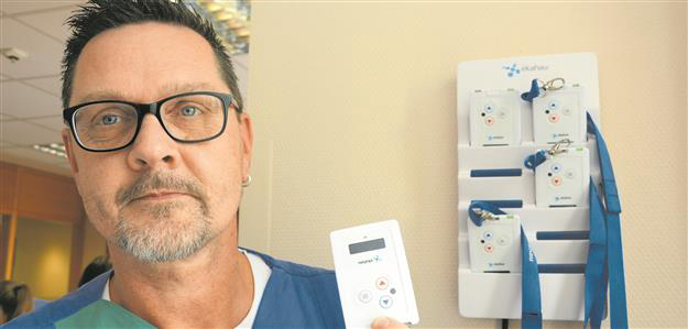 Ein Mann hält ein RTLS-Tag in der Hand, im Hintergrund befindet sich eine an der Wand montierte Ladestation mit weiteren Tags.